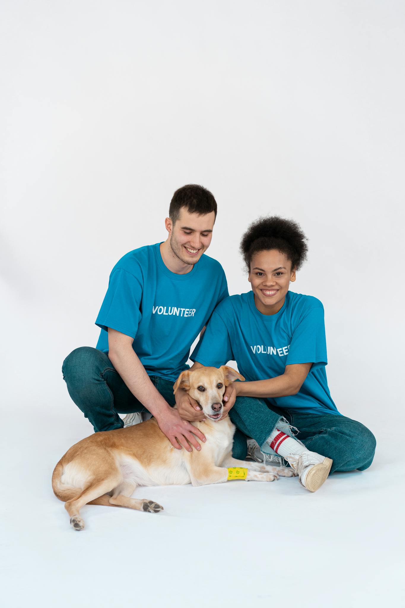 A happy couple of volunteers smiling while posing with a rescue dog in a studio setting.